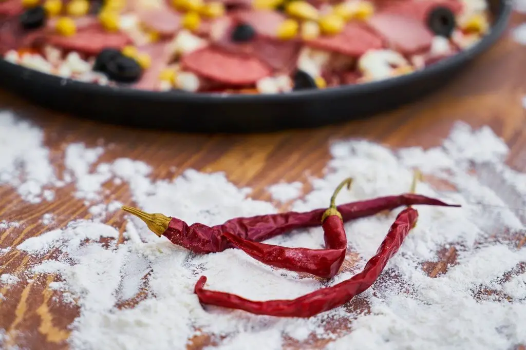 red peppers on flour in front of an uncooked pizza