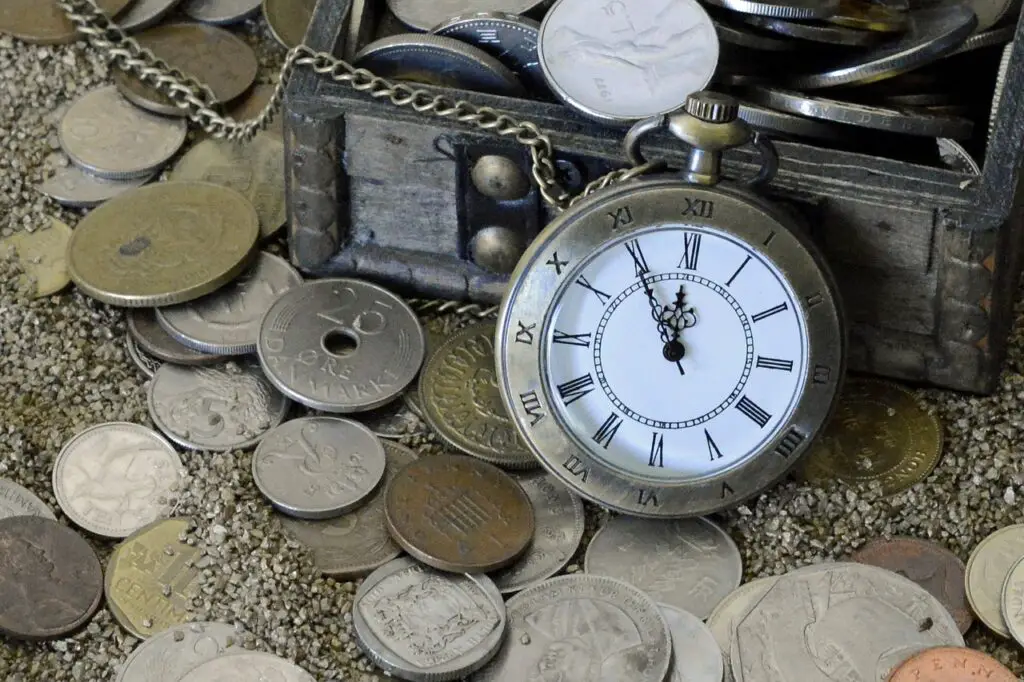 A photograph of a pocket watch leaning against a treasure chest filled with coins to depict the treasure in a D&D heist.
